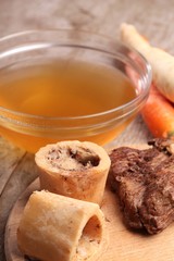 Bowl with beef broth, boiled bones, meat and fresh vegetables.