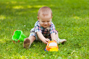 little boy sits on a grass and plays toys