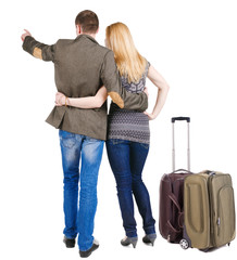 Back view of traveling young couple with  suitcas pointing