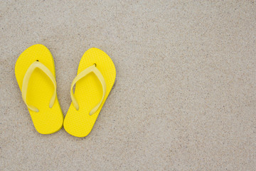 Fototapeta na wymiar yellow flip flops on the beach sand