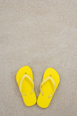 Fototapeta na wymiar yellow flip flops on the white beach sand
