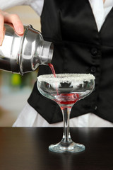 Barmen hand with shaker  pouring cocktail into glass,