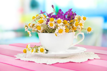 Bouquet of chamomile flowers in cup, on bright background