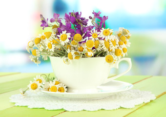 Bouquet of chamomile flowers in cup, on bright background