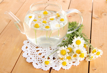 Glass teapot with chamomile on wooden table