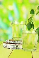 Glasses of birch sap on wooden table, on green background
