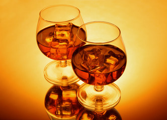 Brandy glasses with ice on yellow background