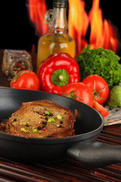 Piece of fried meat on pan on wooden table on fire background