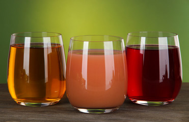 Glasses of fresh juice on table on green background