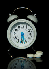 Old style alarm clock  and pills, isolated on black