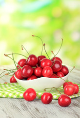 Cherry berries in bowl on wooden table on bright background