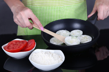 Hands cooking marrows in pan on gray background