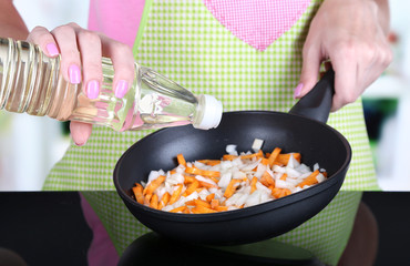 Hands cooking fried onion with carrot in pan in kitchen