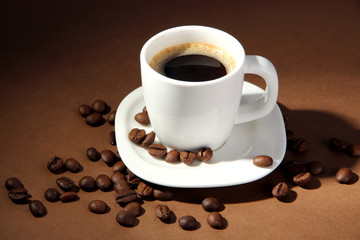 Cup of coffee with coffee beans on brown background