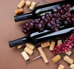 Bottles of wine, grapes and corks on brown background