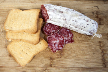 Salame a fette con fette bisocottate su un tagliere di legno