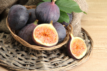 Ripe sweet figs with leaves in basket, on wooden table,