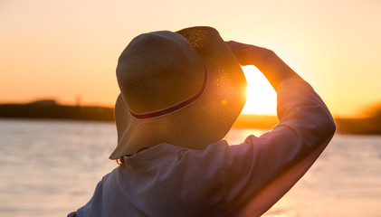 Young and beautiful woman wearing a hat in sunset light looking