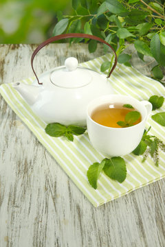 Teapot and cup of herbal tea with fresh mint on wooden table