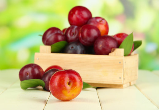 Ripe plums in wooden box on wooden table on natural background