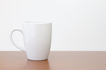 Obraz premium White mug on dark wooden table with white wall