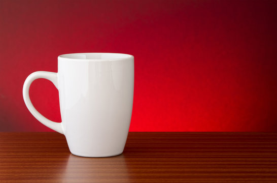White mug on dark wooden table with red motled glow background
