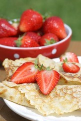 Sweet crepes with strawberries on garden table.