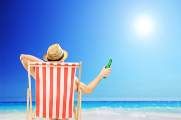 Man with hat sitting on a beach chair and holding a beer