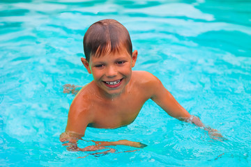 Fototapeta na wymiar Smiling boy swims in pool on summer vacations