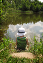 Fototapeta premium child sitting on the bank of a lake on a sunny day