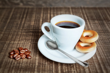 A cup of coffee with baked cracknels, bagels. Coffee beans on th