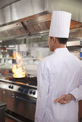Chef with Fingers Crossed as a Pan Catches Fire