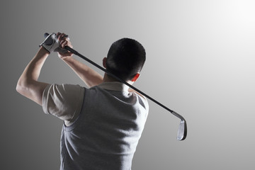 Young golf player swinging, rear view