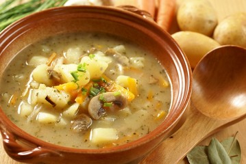 Bowl with potato soup, wooden ladle and food ingredients.