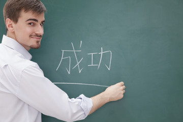 Portrait of smiling male teacher in front of chalkboard writing, Chinese characters
