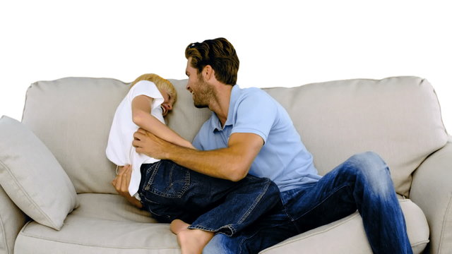 Father tickling his son on the sofa on white background