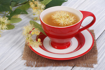 Tea with a linden in a red cup on a wooden table.