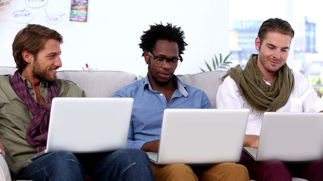 Three colleagues sitting on couch using laptop