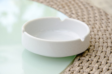 Single white ashtray standing on the glass table of street cafe