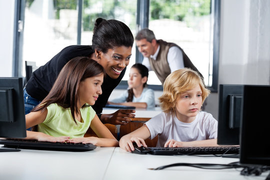 Female Teacher Assisting Schoolchildren In Using Computer