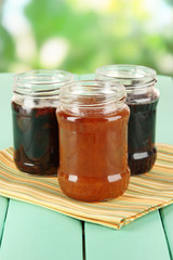 Tasty jam in banks on table on bright background