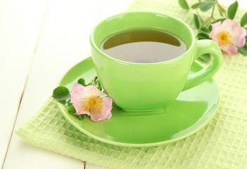 Cup of herbal tea with hip rose flowers on white wooden table