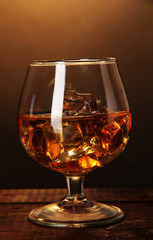 Brandy glass with ice on wooden table on brown background