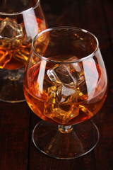 Brandy glasses with ice on wooden background