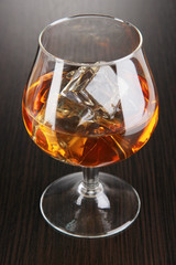 Brandy glass with ice on wooden background