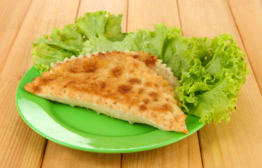 Tasty chebureks with fresh herbs on plate,on wooden background