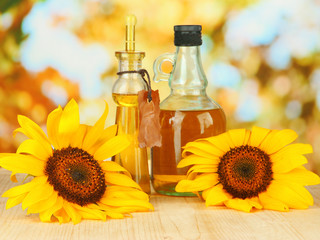 Oil in jars and sunflower on wooden table close-up