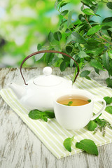 Teapot and cup of herbal tea with fresh mint on wooden table