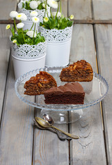 Chocolate cake on glass stand, on grey wooden table. Daisy flowe