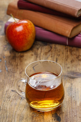 Glass of hot steaming tea on wooden table. Pile of books and red